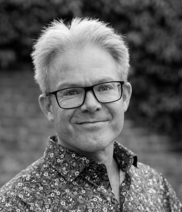 Black and white image of board member, Guy Parker smiling towards the camera 