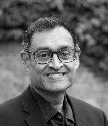 Black and white image of board member, Girish Menon smiling towards the camera